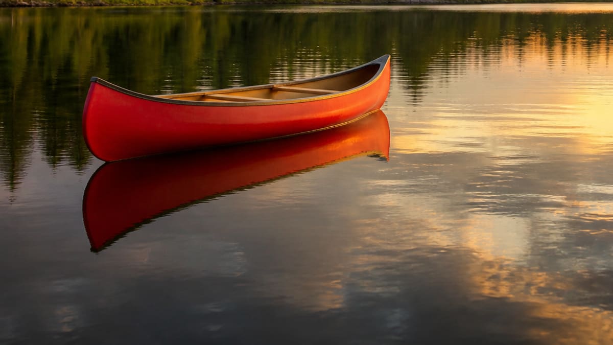 The same red canoe after a tighter crop on the pine lake, boat and reflection filling the frame.