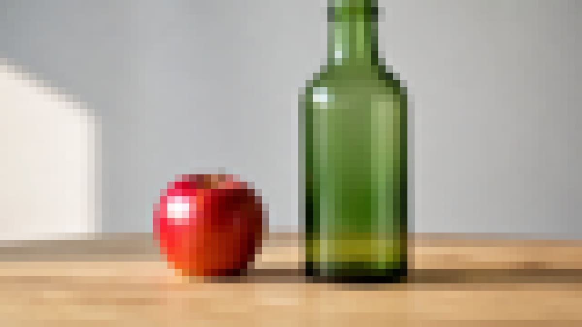 The same red apple and green bottle after a whole-image pixelate mosaic.